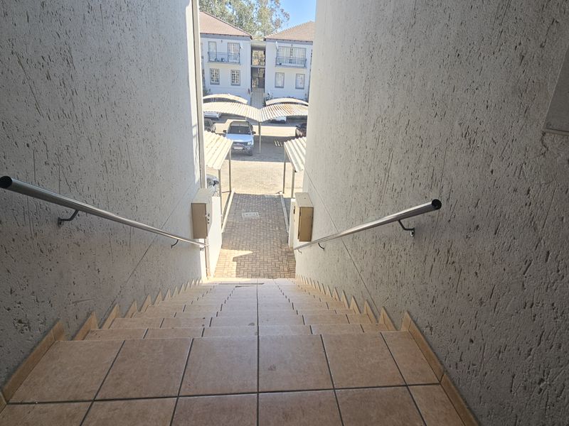 Exterior staircase with metal handrails leading down to a paved walkway and communal carport area within the apartment complex.