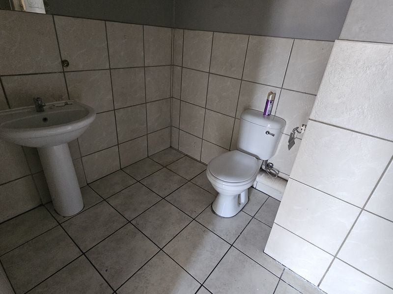 A functional bathroom featuring a pedestal basin and ceramic toilet with full-height wall tiling and floor tiles.