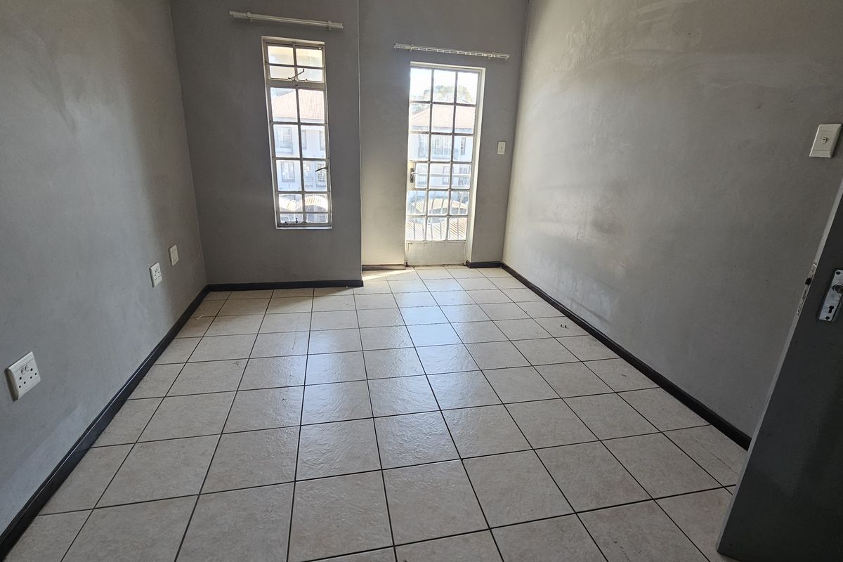 An empty bedroom featuring tiled flooring, neutral grey walls, and a glass panel door leading to an exterior space.