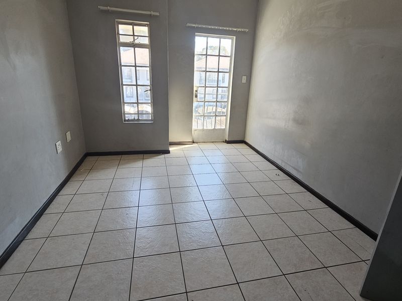 An empty bedroom featuring tiled flooring, neutral grey walls, and a glass panel door leading to an exterior space.