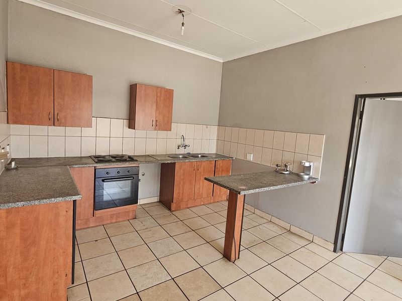 A functional kitchen featuring wood-finish cabinetry, granite countertops, a built-in oven and hob, and tiled flooring, offering a blank canvas for renovation.
