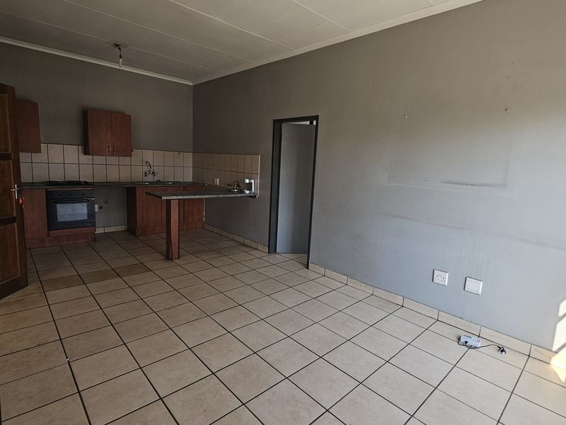 An open-plan kitchen and living area featuring tiled flooring, built-in cabinetry with granite countertops, and an integrated oven, offering a blank canvas for customization.