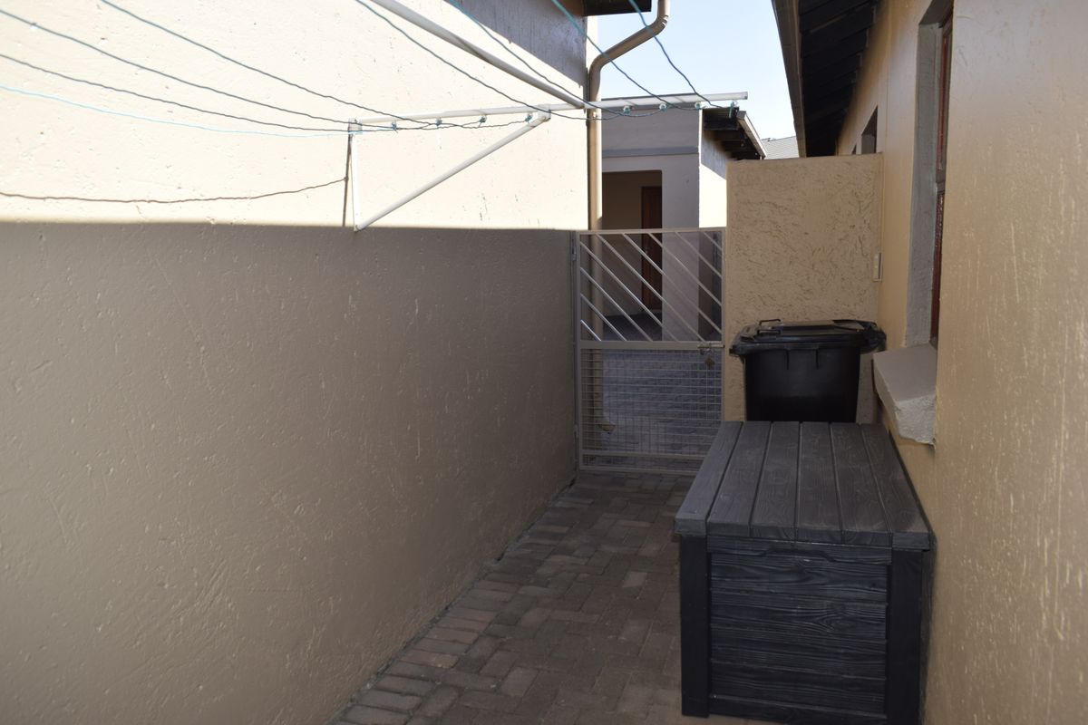 A paved side passage or rear courtyard area featuring a secure metal gate, boundary wall, and wall-mounted clothesline.