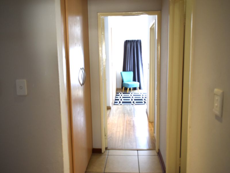 A functional hallway connecting living spaces, featuring built-in cupboard storage, tiled flooring, and a transition to laminate flooring in the adjacent room.