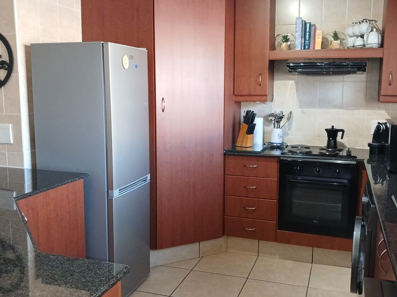 A functional kitchen featuring dark granite countertops, wood-finish cabinetry, built-in oven with hob, and tiled flooring.