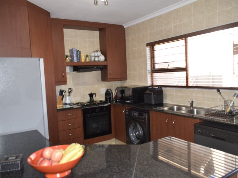 A functional kitchen featuring dark wood cabinetry, granite countertops, a double basin sink, and built-in cooking appliances with a tiled backsplash.