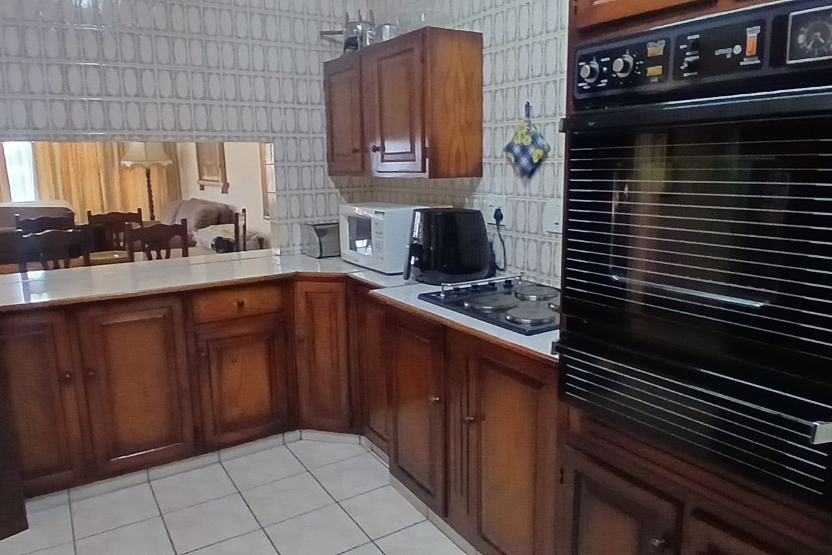 A functional kitchen featuring traditional wooden cabinetry, a built-in wall oven, electric hob, and a convenient serving hatch opening into the living area.