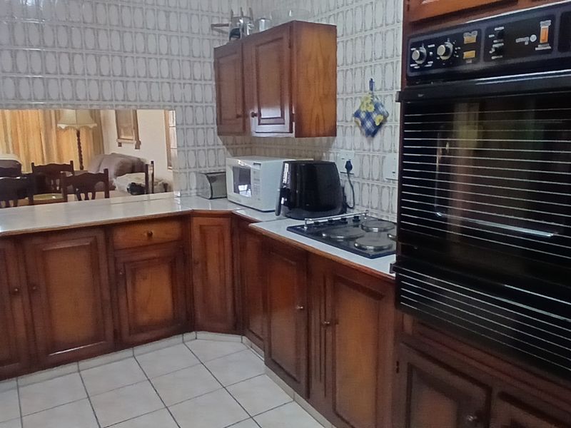 A functional kitchen featuring traditional wooden cabinetry, a built-in wall oven, electric hob, and a convenient serving hatch opening into the living area.