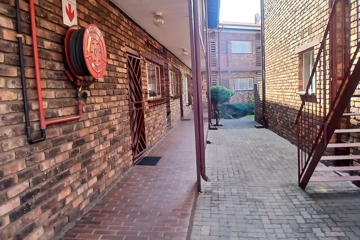 Exterior walkway of a townhouse complex featuring exposed brick walls, a fire hose reel, and a metal staircase leading to upper levels.
