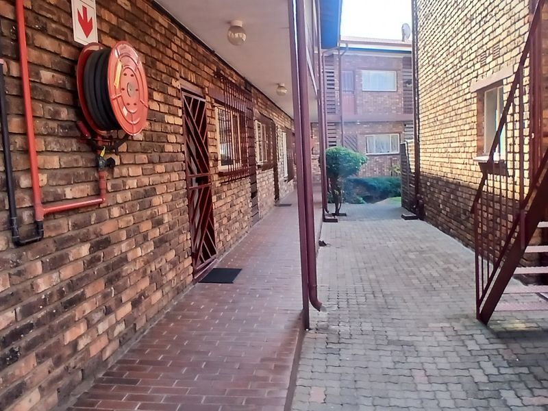 Exterior walkway of a townhouse complex featuring exposed brick walls, a fire hose reel, and a metal staircase leading to upper levels.