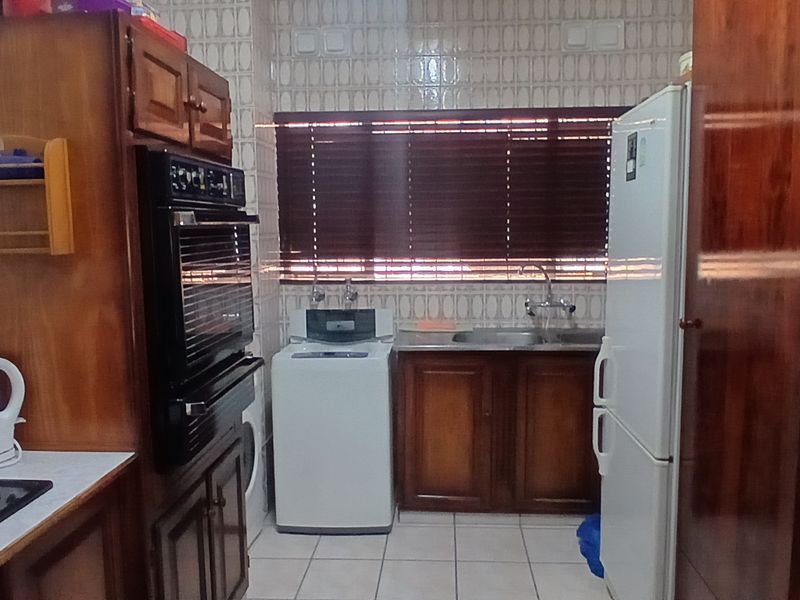 A functional kitchen featuring traditional wooden cabinetry, built-in oven, electric hob, and tiled finishes, offering a classic layout with ample storage space.