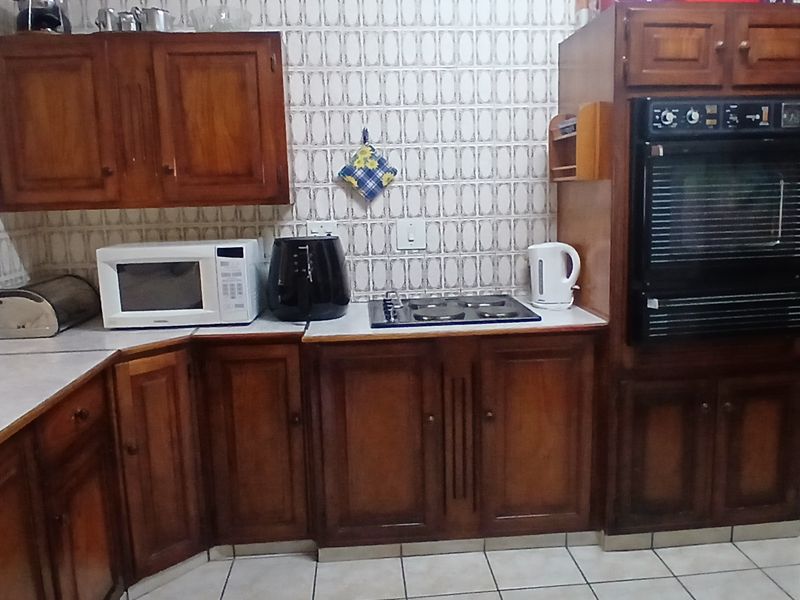 A dated kitchen featuring traditional wooden cabinetry, built-in oven, electric hob, and tiled finishes throughout.