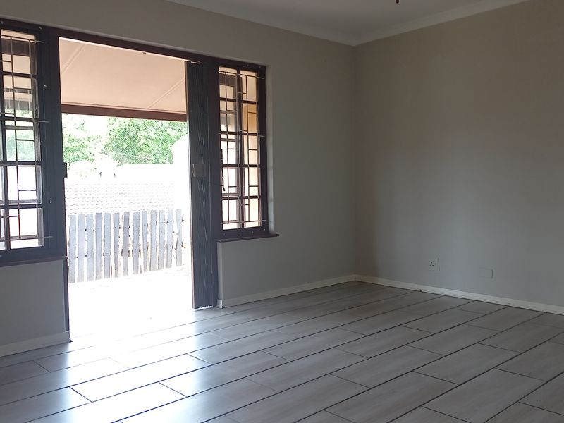 An empty living room featuring light-toned tiled flooring and a sliding door with security bars leading to an outdoor area.