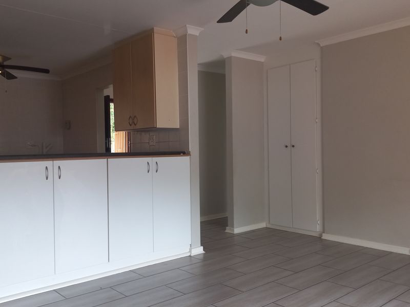 An open-plan living and kitchen area featuring modern laminate flooring, neutral walls, built-in cabinetry, and ceiling fans in a clean, vacant space.