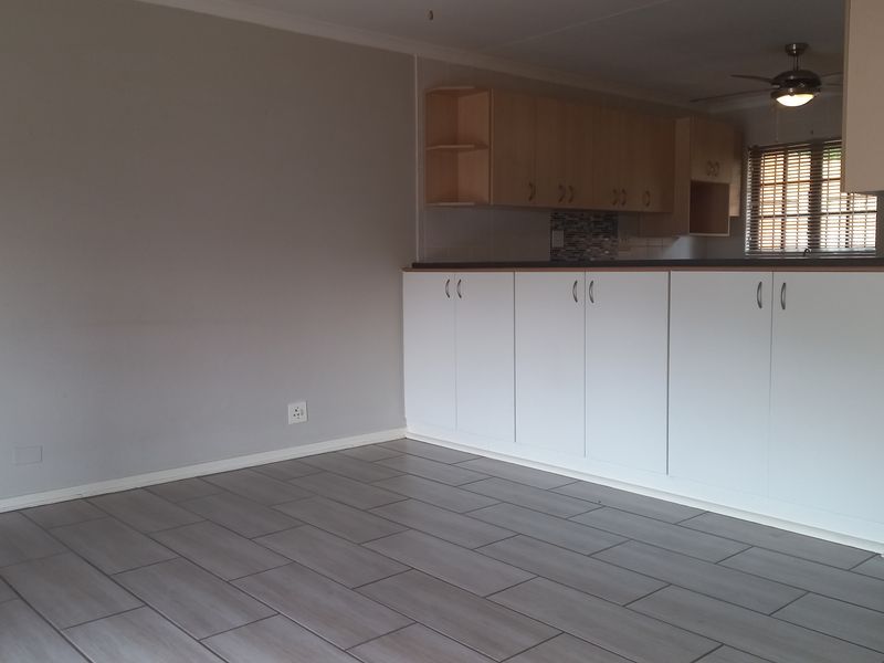 An open-plan living and kitchen area featuring modern grey tiled flooring, built-in cabinetry, and a ceiling fan in a neutral, well-maintained space.