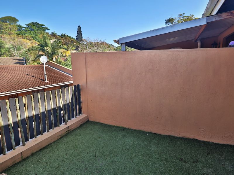 A compact outdoor patio area featuring artificial grass, a timber boundary fence, and a masonry wall, providing a private space for outdoor relaxation.