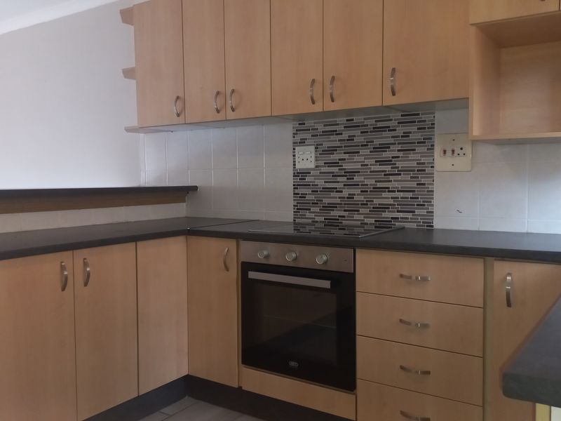 Functional kitchen featuring light wood-tone cabinetry, dark laminate countertops, a built-in oven with electric cooktop, and a decorative mosaic tile backsplash.