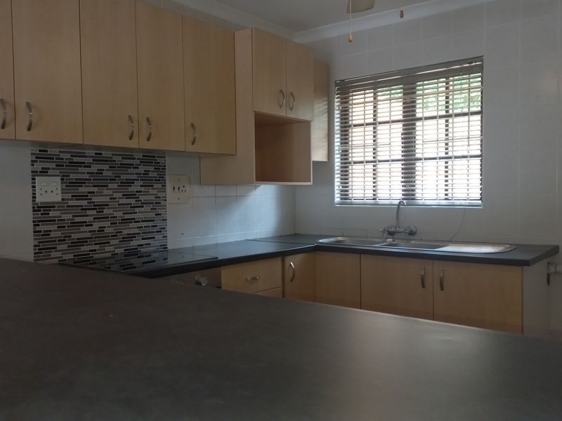 A functional kitchen featuring light wood-tone cabinetry, dark laminate countertops, a mosaic tile backsplash, and a double bowl stainless steel sink.