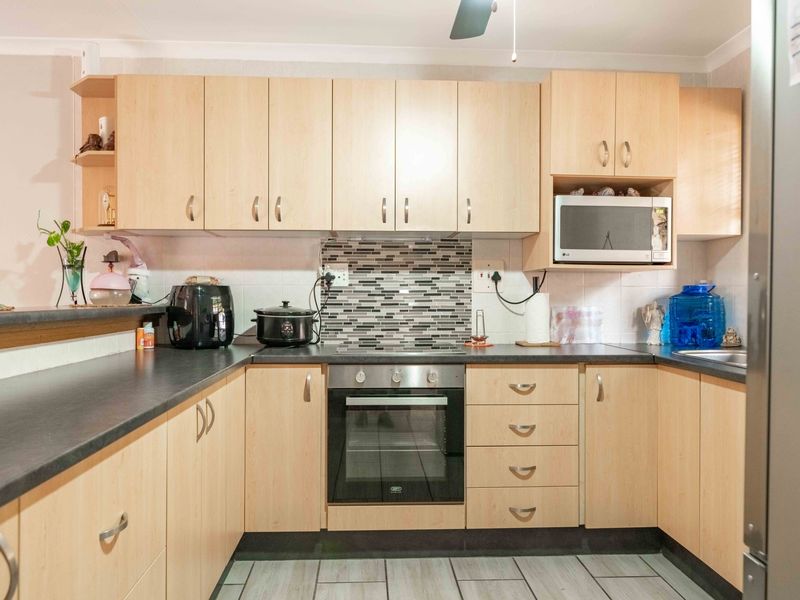 Functional kitchen featuring light wood-finish cabinetry, dark laminate countertops, a built-in oven with hob, and a decorative mosaic tile splashback.