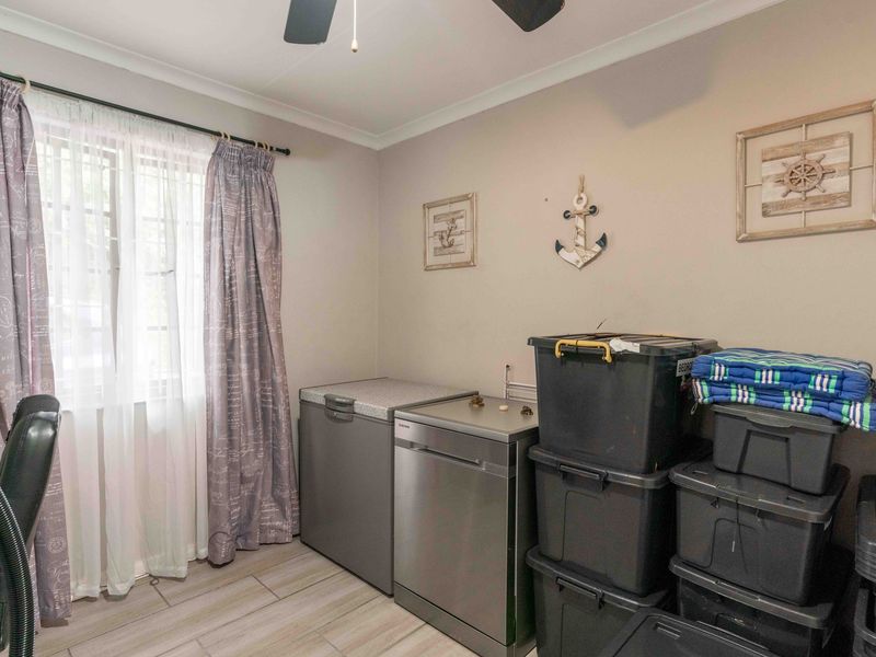 A functional utility space featuring tiled flooring and a ceiling fan, currently utilized for storage and appliance placement.