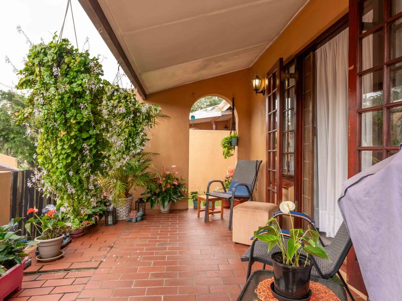A covered patio area featuring terracotta tiled flooring, an arched architectural detail, and timber-framed glass doors providing access to the interior.