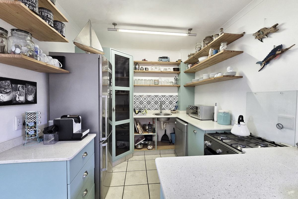 A compact kitchen featuring light blue cabinetry, stone countertops, open wooden shelving, a gas stove, and decorative tiled backsplash.