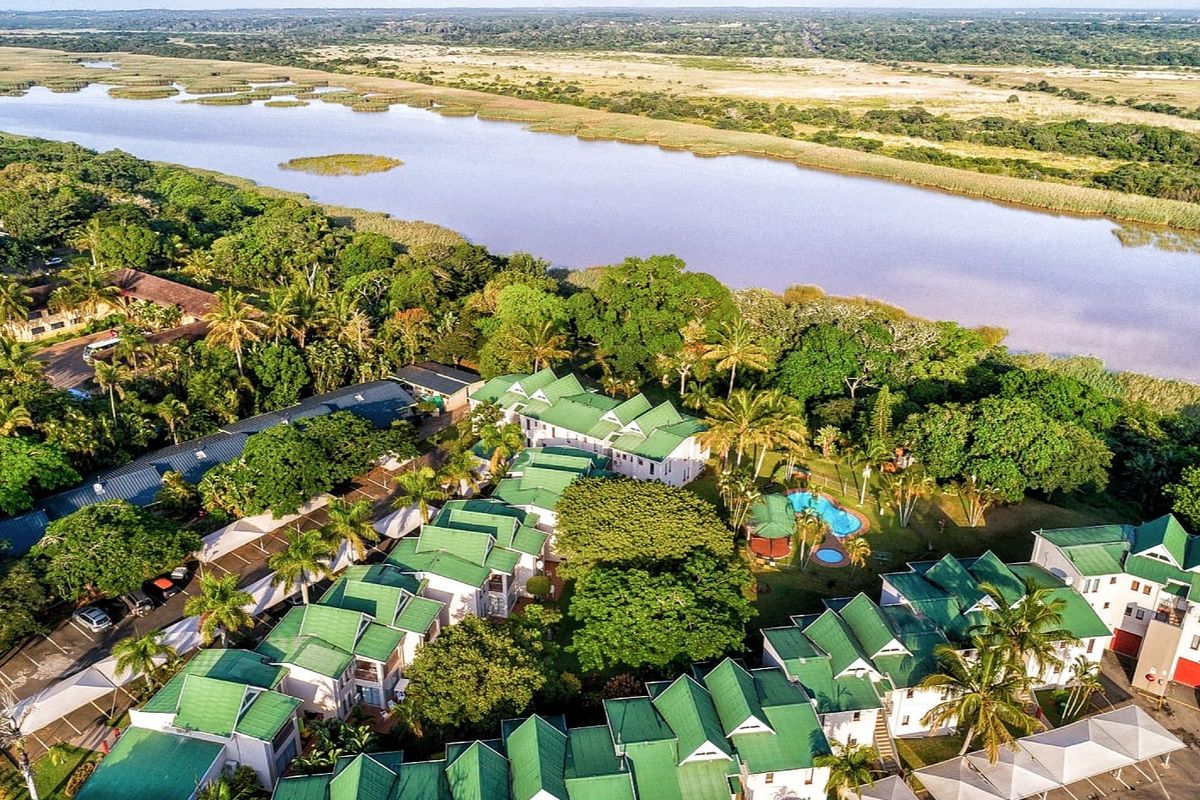 Aerial view of a residential apartment complex featuring green roofs, a swimming pool, and landscaped grounds situated near a river.