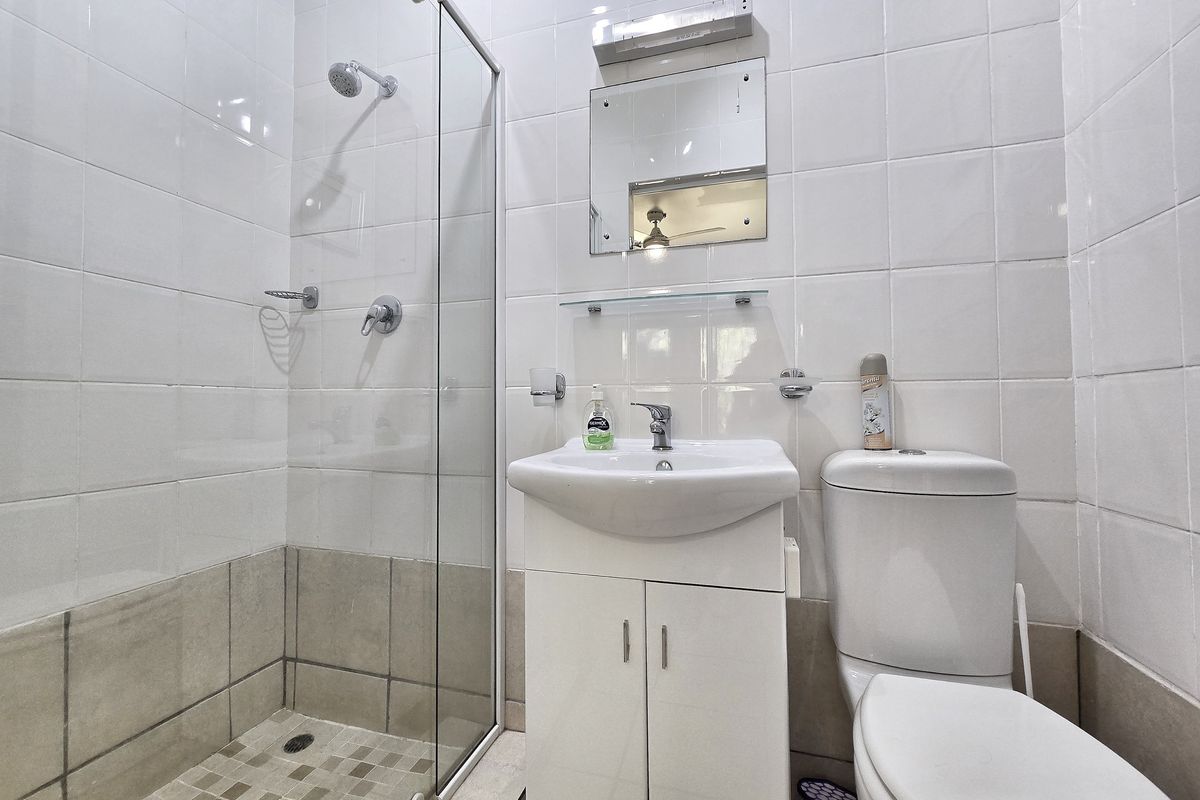 A clean, functional bathroom featuring a glass-enclosed shower, vanity basin with storage cabinet, and a standard toilet with white wall tiling.