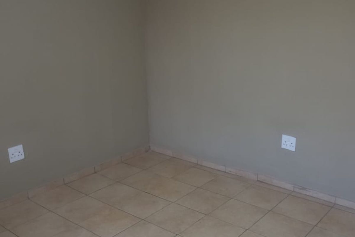 A vacant bedroom featuring neutral wall paint, ceramic floor tiles, and standard electrical outlets, providing a clean and versatile space ready for customization.