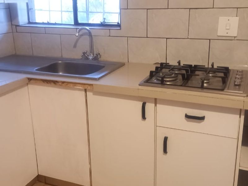 A compact kitchen featuring a stainless steel sink, gas hob, tiled backsplash, and built-in cabinetry with laminate countertops.