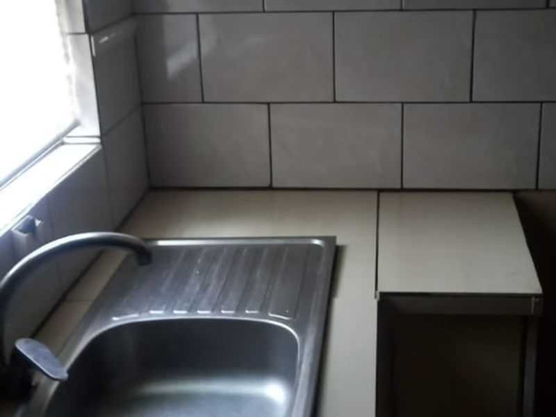 A compact kitchen area featuring a stainless steel sink, tiled splashback, and functional upper and lower cabinetry.
