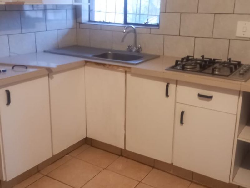 A compact kitchen featuring white base cabinetry, laminate countertops, a built-in gas hob, and a stainless steel sink with tiled backsplash.