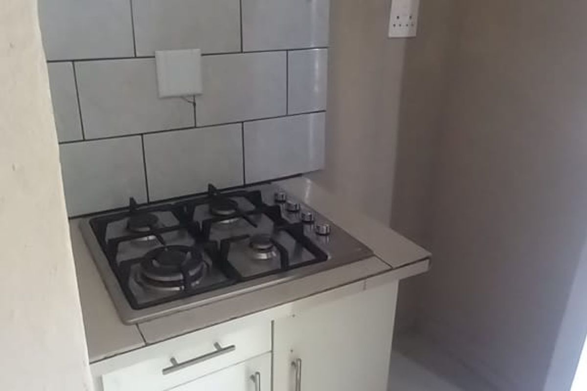 Compact kitchen area featuring a built-in gas hob, tiled splashback, and white base cabinetry with tiled flooring.
