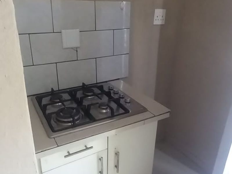 Compact kitchen area featuring a built-in gas hob, tiled splashback, and white base cabinetry with tiled flooring.
