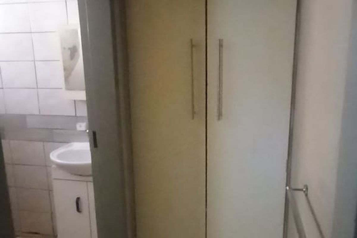A small bathroom area featuring a vanity basin, built-in storage cupboard, and tiled finishes, requiring cosmetic updates to improve its overall condition.