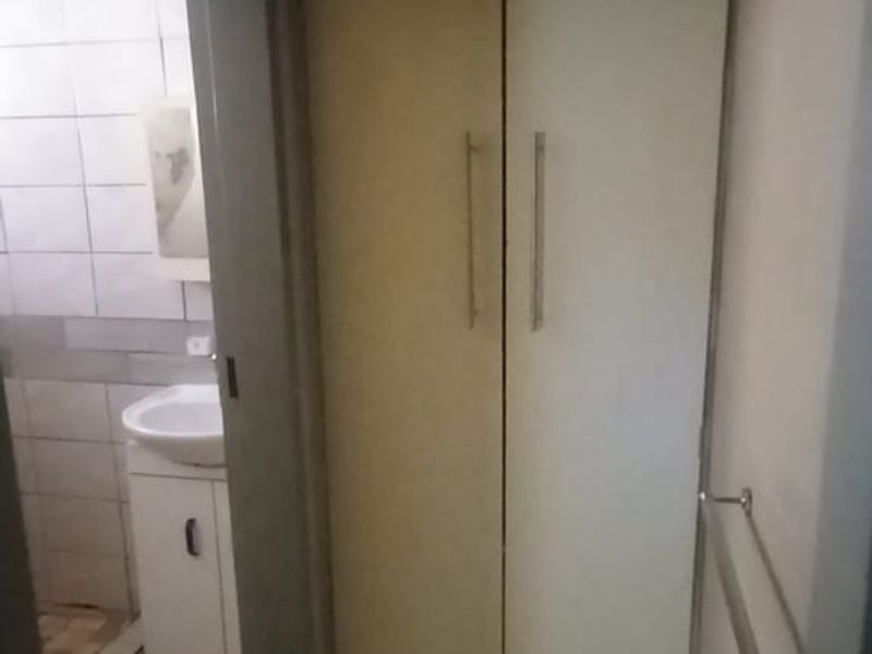 A small bathroom area featuring a vanity basin, built-in storage cupboard, and tiled finishes, requiring cosmetic updates to improve its overall condition.