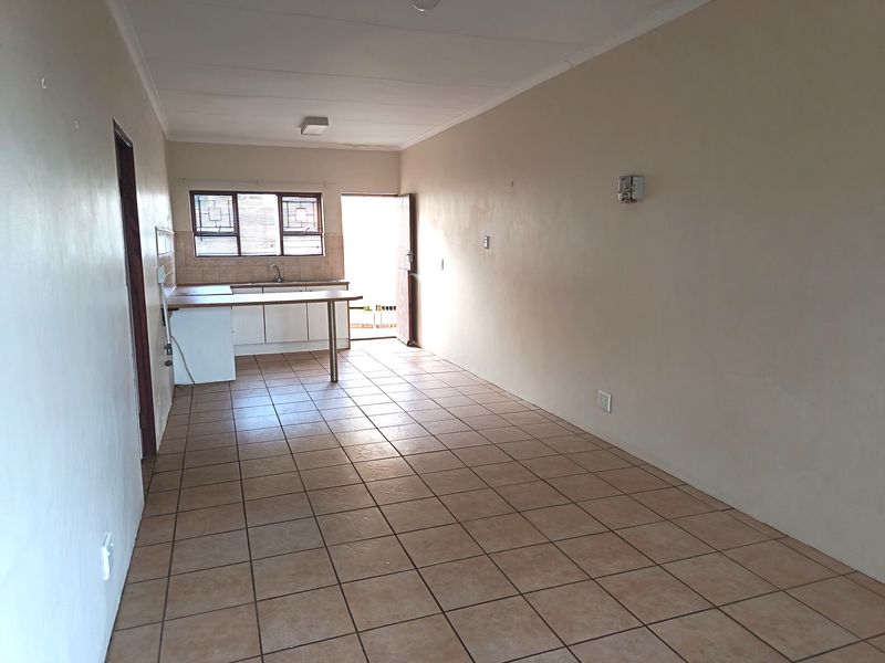 An open-plan living and kitchen area featuring tiled flooring, built-in cabinetry, and a breakfast counter, leading to an exterior doorway.