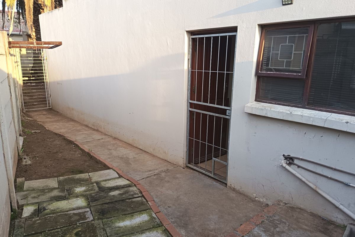 Rear exterior view of the property featuring a paved walkway, security gate, and boundary wall with visible signs of wear on the exterior finishes.