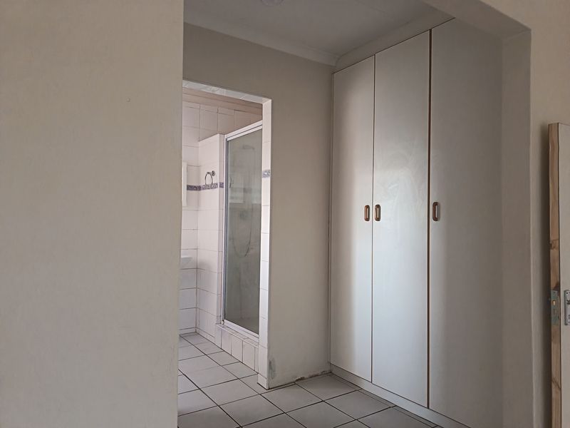 A bedroom area featuring built-in cupboards and an adjoining en-suite bathroom with a shower cubicle and tiled flooring.