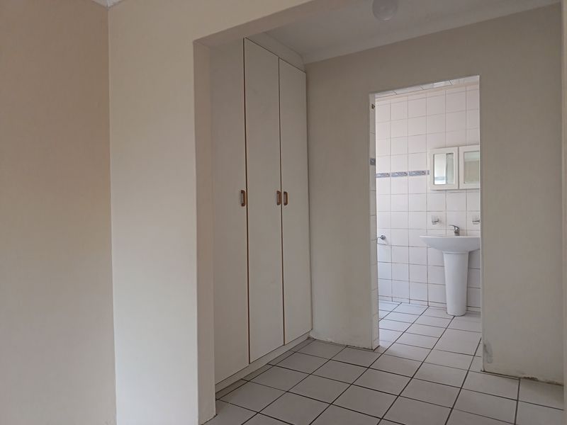 A functional bathroom featuring a pedestal basin, tiled surfaces, and built-in storage cupboards, presenting a clean and neutral space ready for updates.