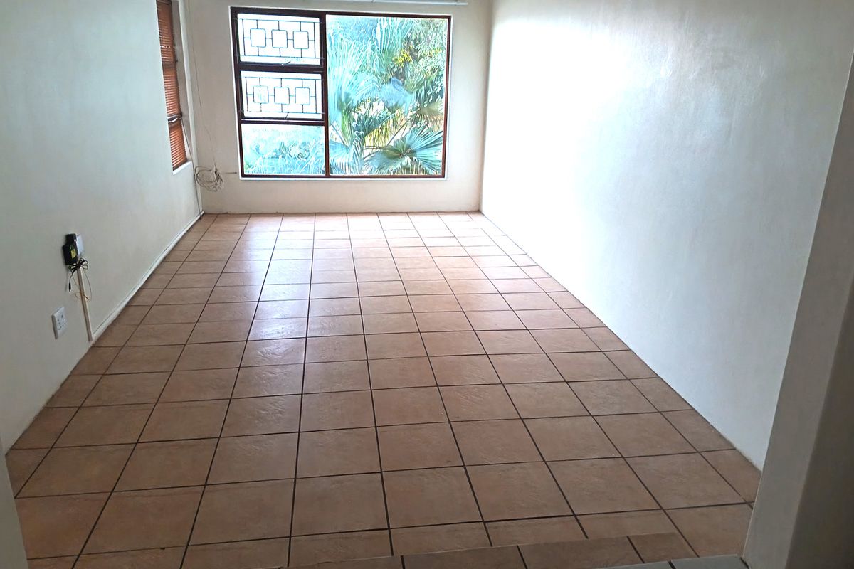 An empty living room featuring ceramic floor tiles, large windows with security bars, and neutral wall finishes, offering a blank canvas for interior design.