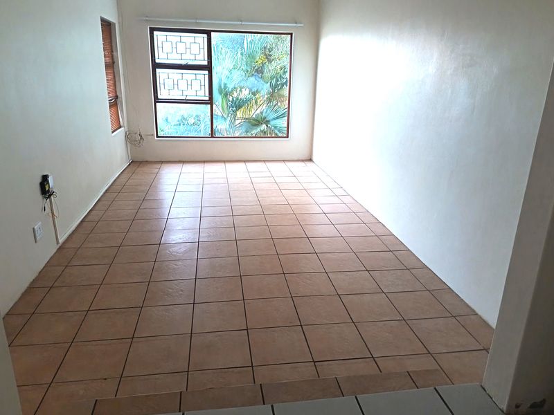An empty living room featuring ceramic floor tiles, large windows with security bars, and neutral wall finishes, offering a blank canvas for interior design.