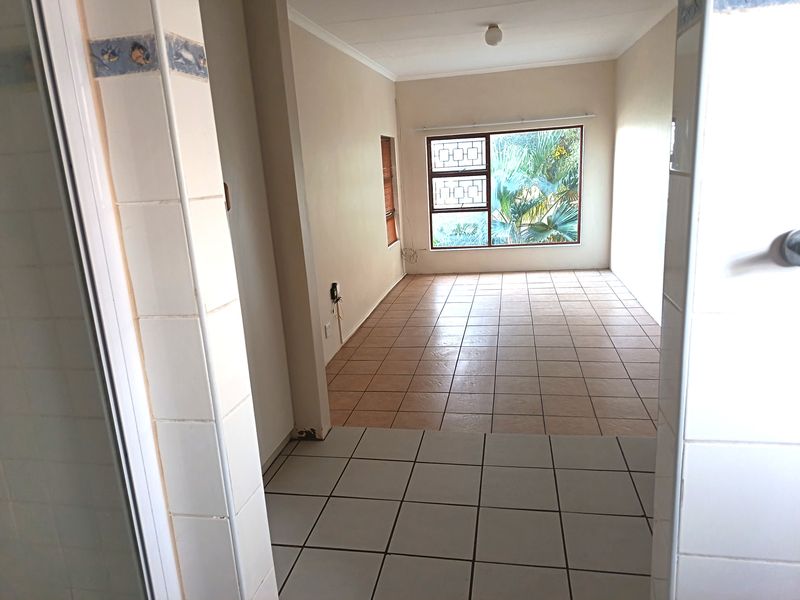 An empty, tiled living area with natural light, featuring security bars on the window and requiring minor cosmetic repairs.