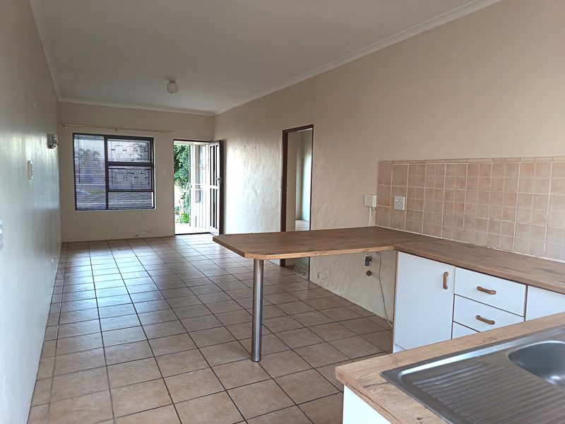 Open-plan living and kitchen area featuring tiled flooring, a breakfast bar, and functional cabinetry, offering a blank canvas for modern interior design.