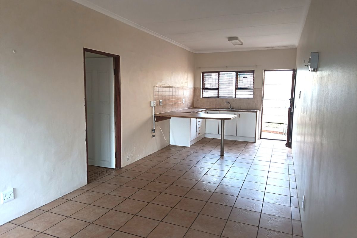 An empty kitchen featuring tiled flooring, built-in cabinetry, a breakfast counter, and a tiled splashback with direct access to an outdoor area.