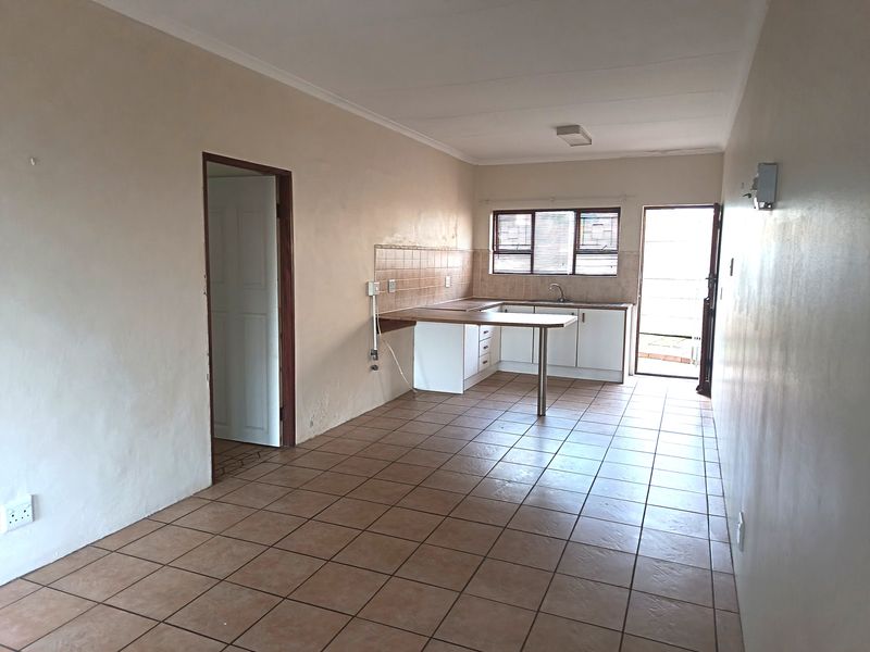 An empty kitchen featuring tiled flooring, built-in cabinetry, a breakfast counter, and a tiled splashback with direct access to an outdoor area.