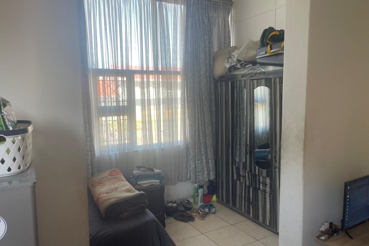 A bedroom featuring tiled flooring and a large window with security bars, currently used for storage.