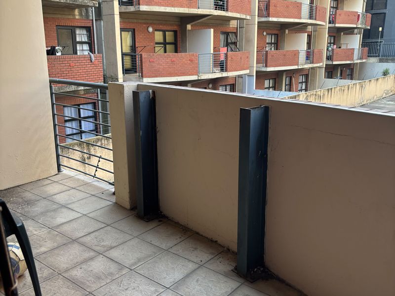 A spacious apartment balcony featuring tiled flooring, metal balustrades, and structural steel columns, overlooking the surrounding residential complex.