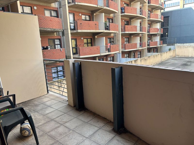 A functional balcony space featuring tiled flooring, a metal balustrade, and a concrete parapet wall, overlooking the apartment complex courtyard.