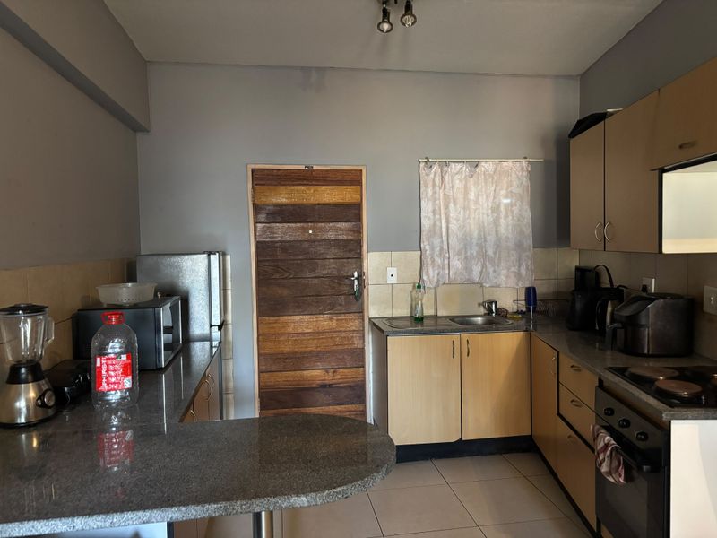 Functional kitchen featuring granite countertops, built-in oven, electric hob, and laminate cabinetry with a tiled backsplash and floor.